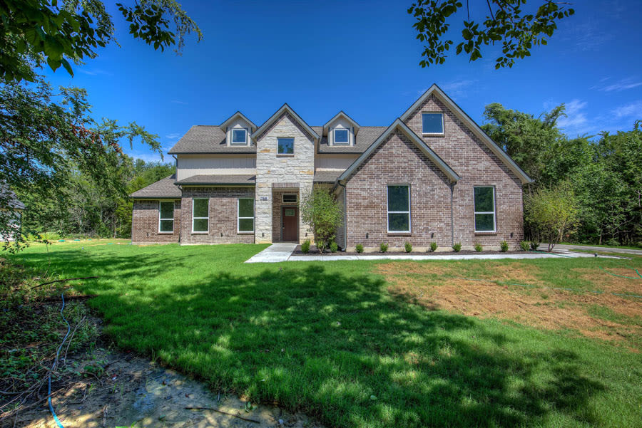 Custom two-story home exterior in Terrell — brick and stone facade with dark shingle roof and landscaped lawn